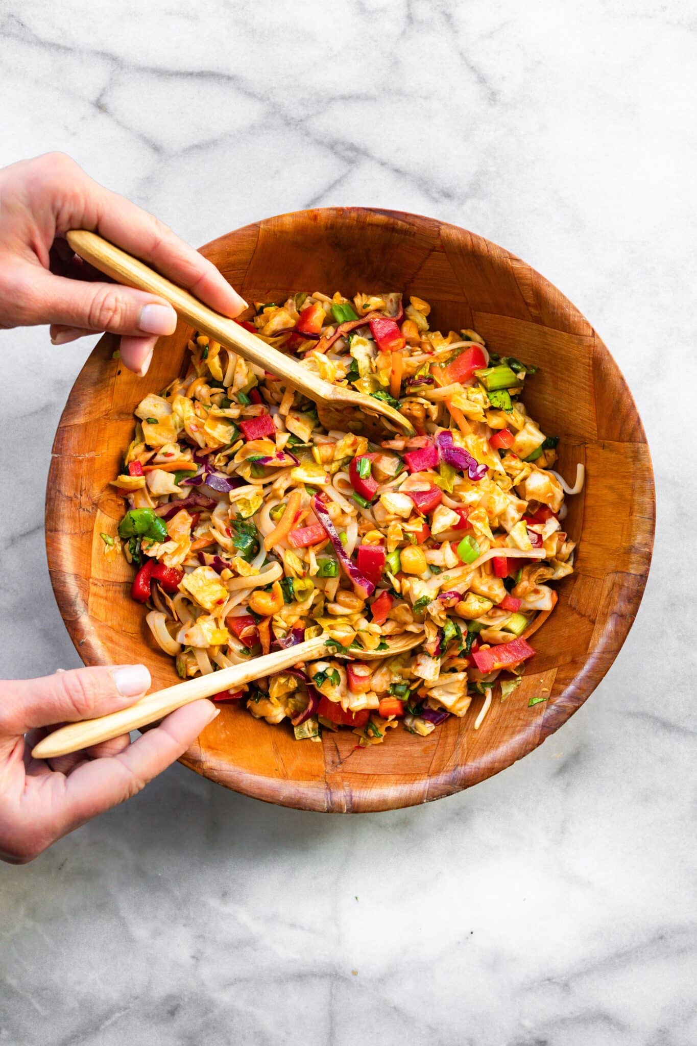 A woman's hands stirring a gluten free Thai noodle salad in a wooden bowl.