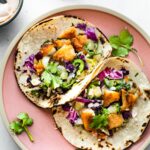 A plate of two gluten-free air fryer fish tacos topped with pineapple slaw, jalapeño slices, and cilantro.