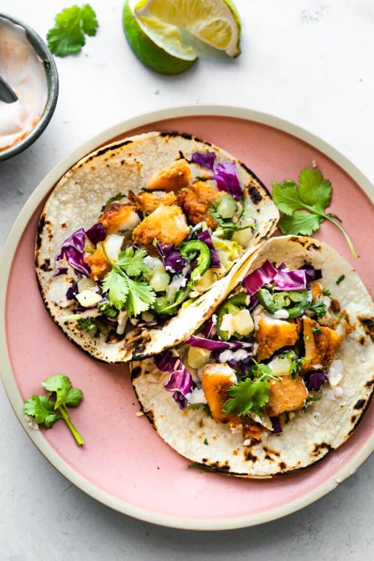 A plate of two gluten-free air fryer fish tacos topped with pineapple slaw, jalapeño slices, and cilantro.