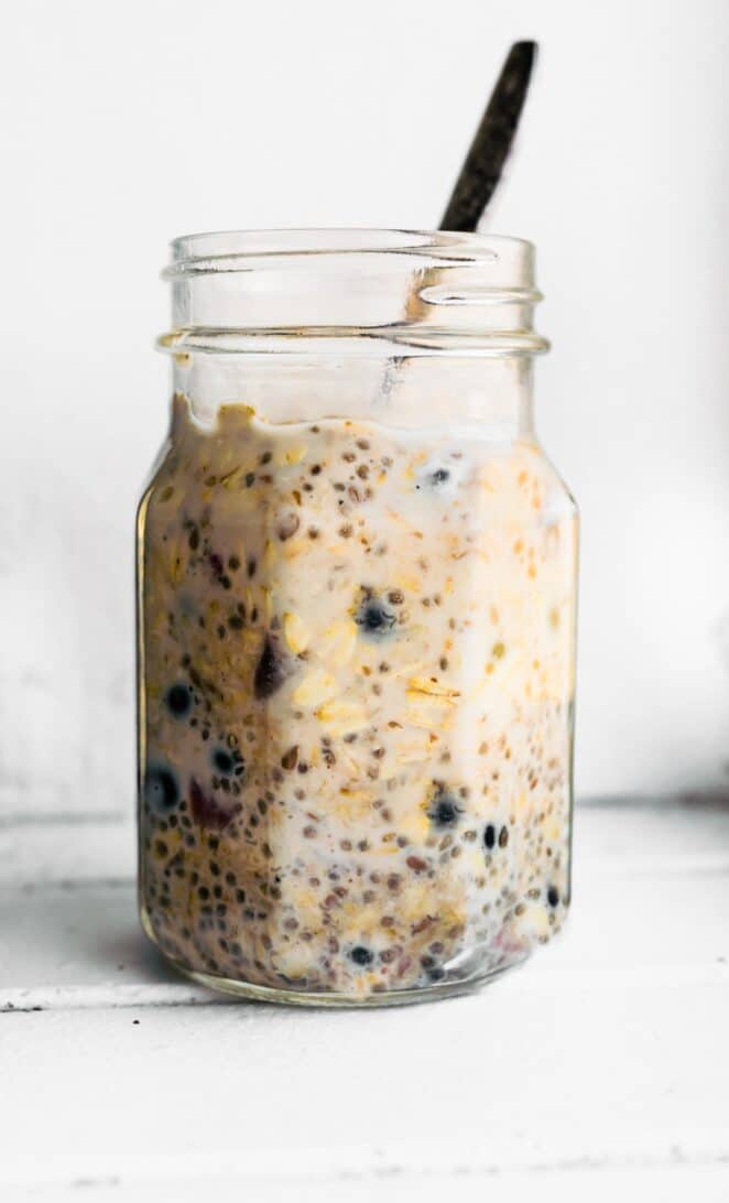Jar of prepared blueberry overnight oats with chia seed and spoon in the middle