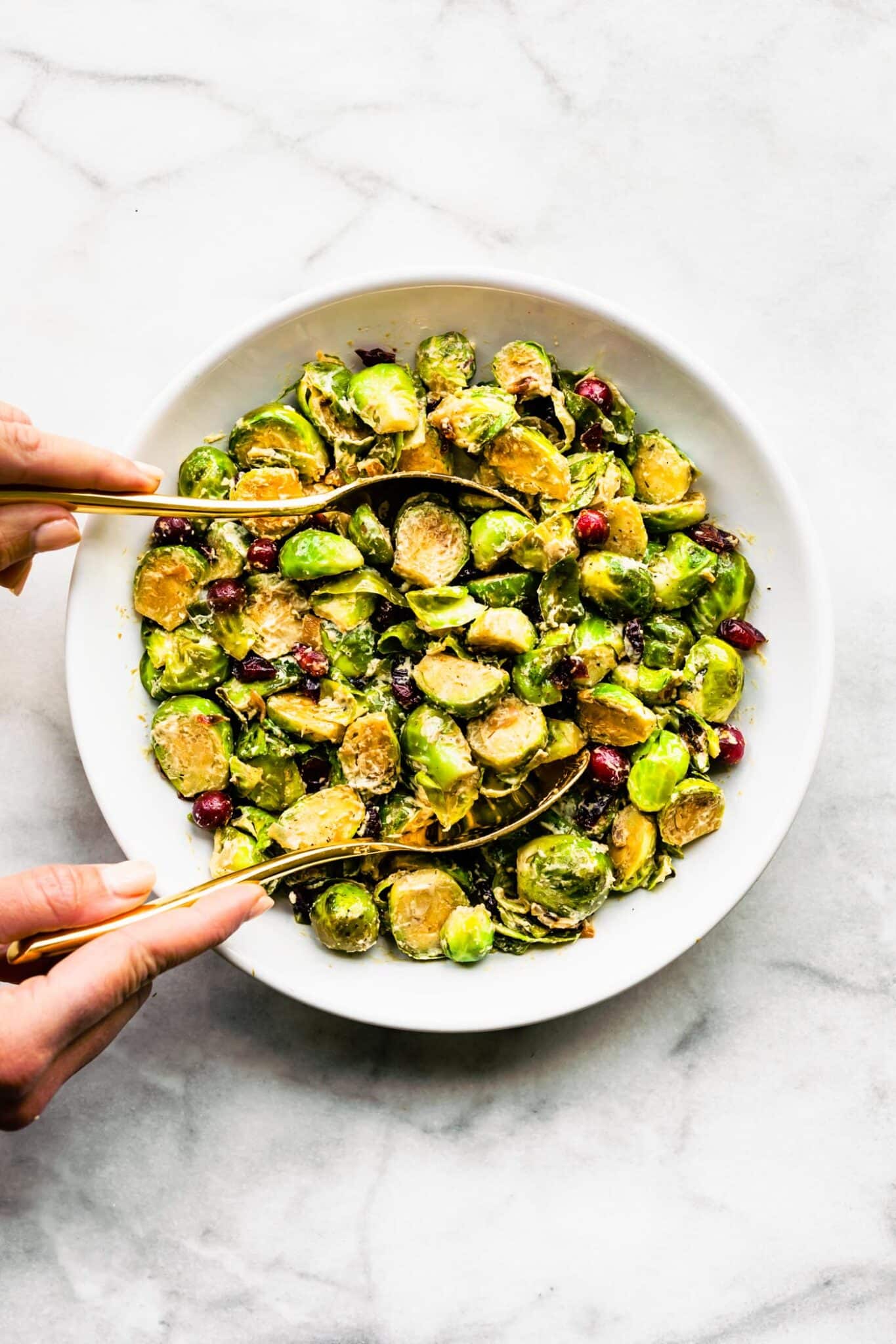 A woman using spoons to scoop out brussels sprout salad from a serving bowl.