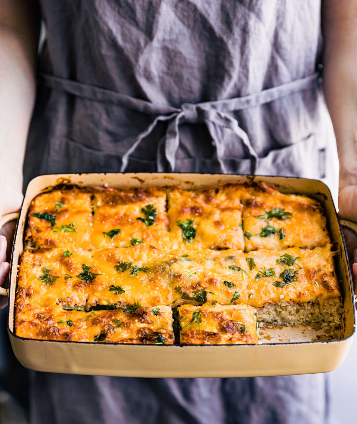 a woman holding a casserole dish filled with tex-mex egg and cauliflower casserole with one piece missing