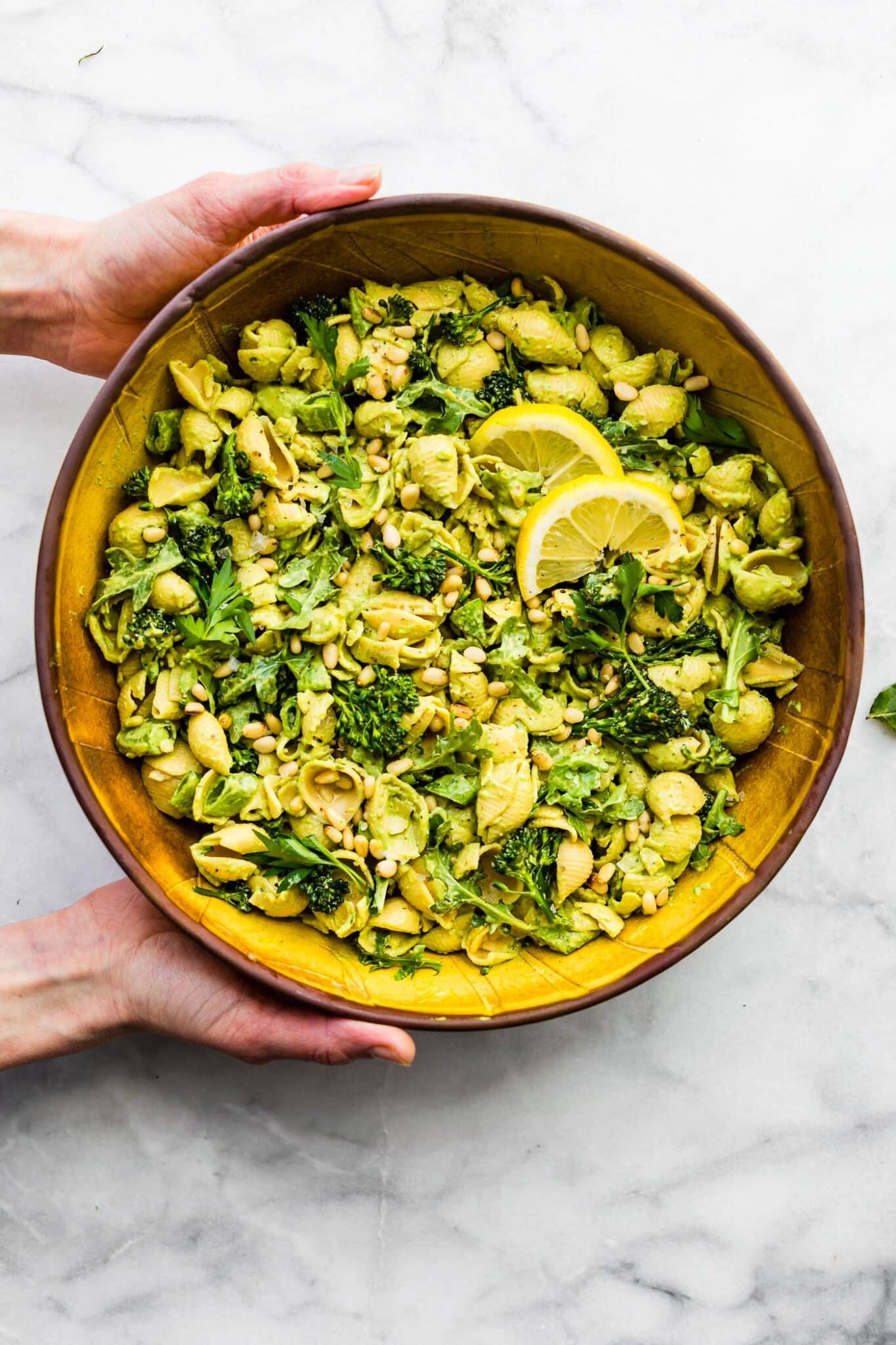 Overhead image of a woman's hands holding a green goddess pasta salad.