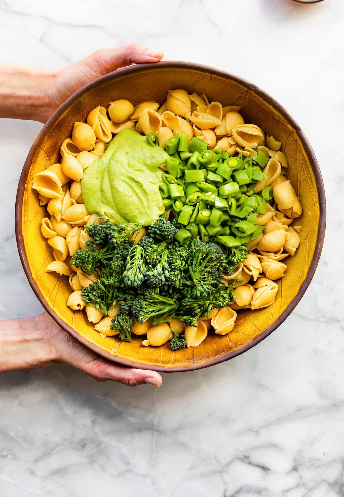 Overhead image of a woman's hands holding unmixed ingredients for a green goddess pasta salad.