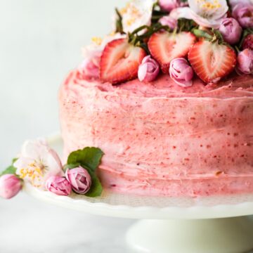 Up close photo of a gluten free strawberry cake topped with fresh flowers and strawberries.