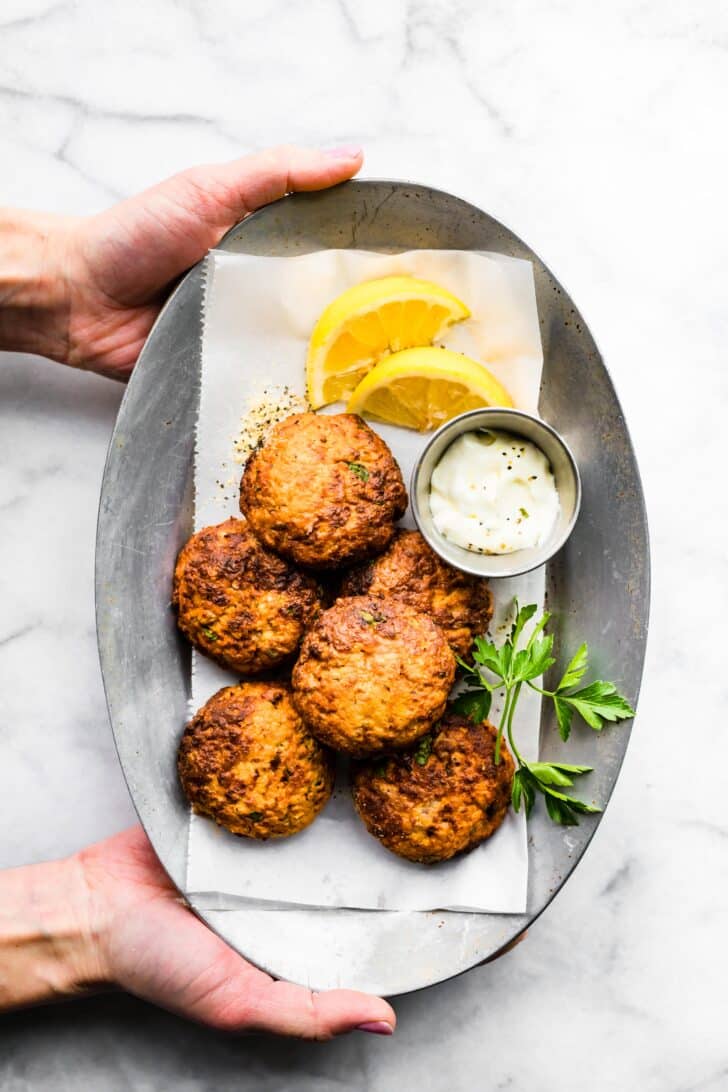 A woman's hands holding a platter of easy tuna patties garnished with lemon and herbs.