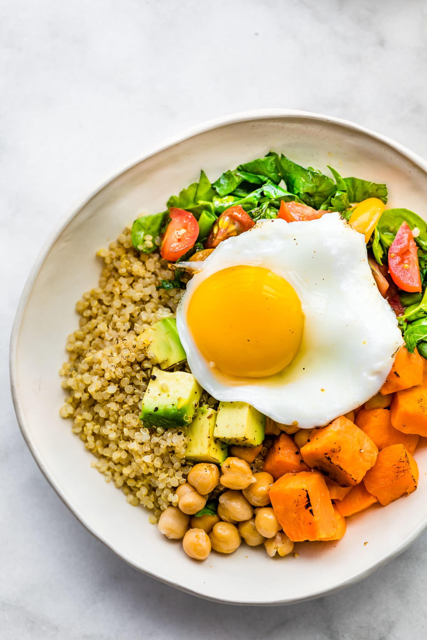 overhead image of a savory quinoa breakfast bowl with quinoa, chickpeas, sweet potatoes, spinach, tomatoes, avocado, and a fried egg