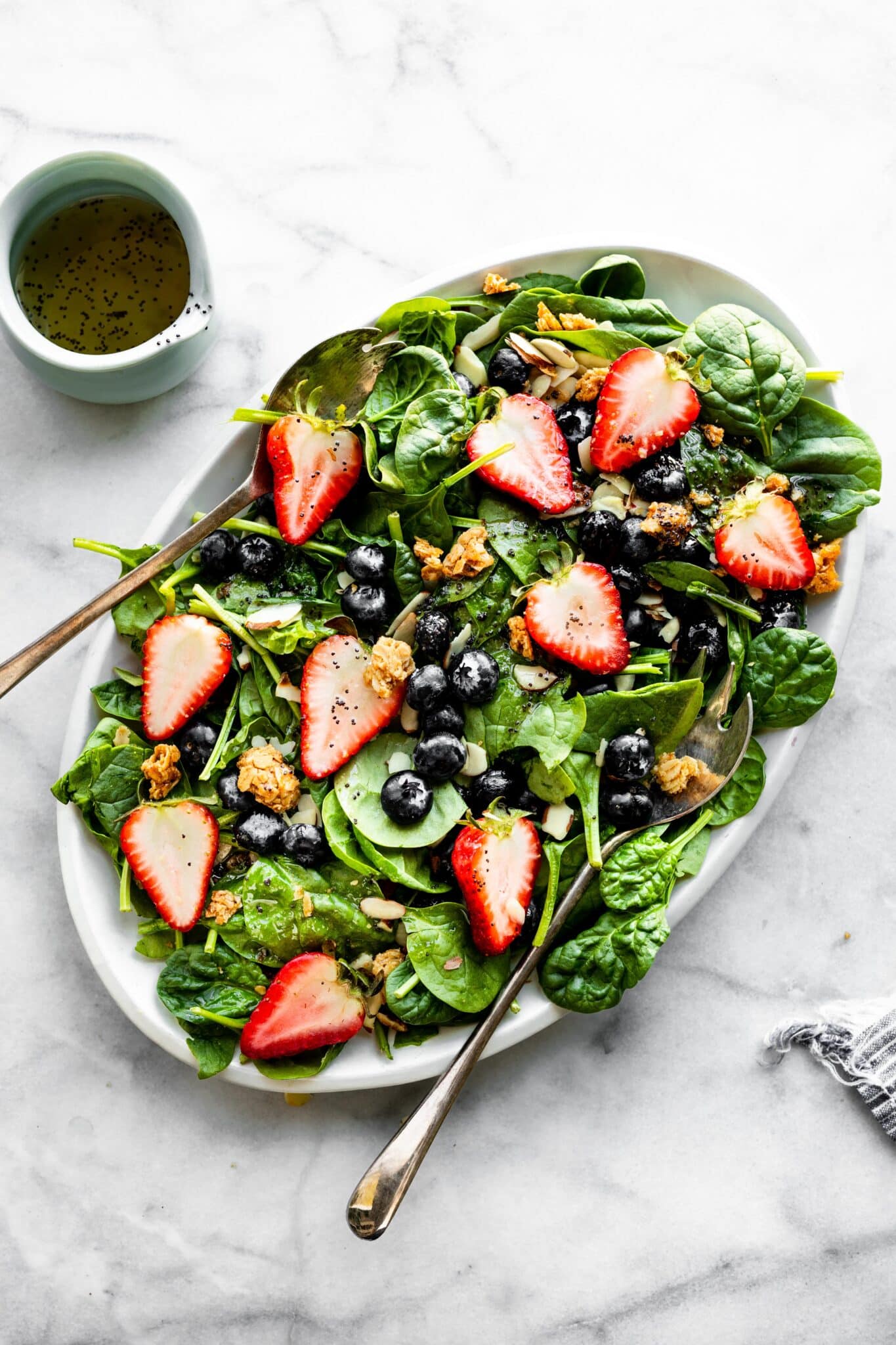 Overhead photo of a spinach salad on a white platter topped with berries and croutons.
