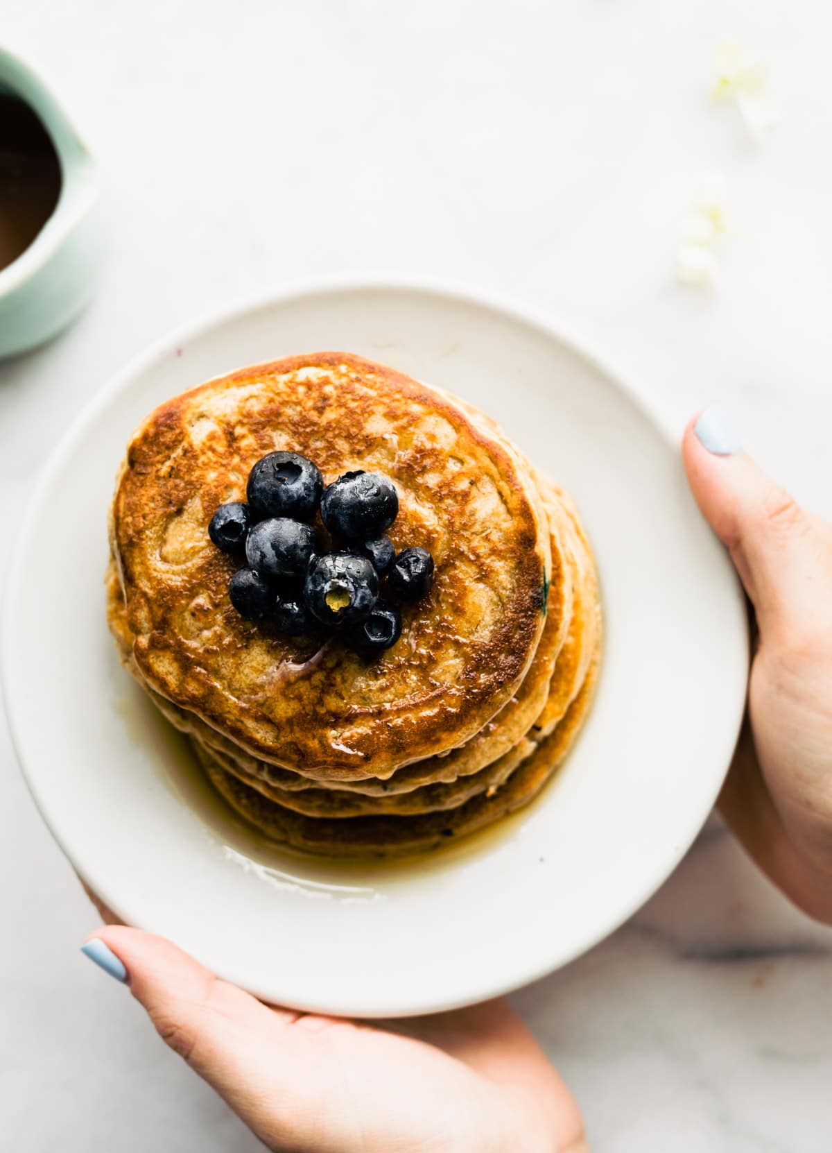 overhead shot: vegan protein pancakes topped with fresh blueberries on white plate