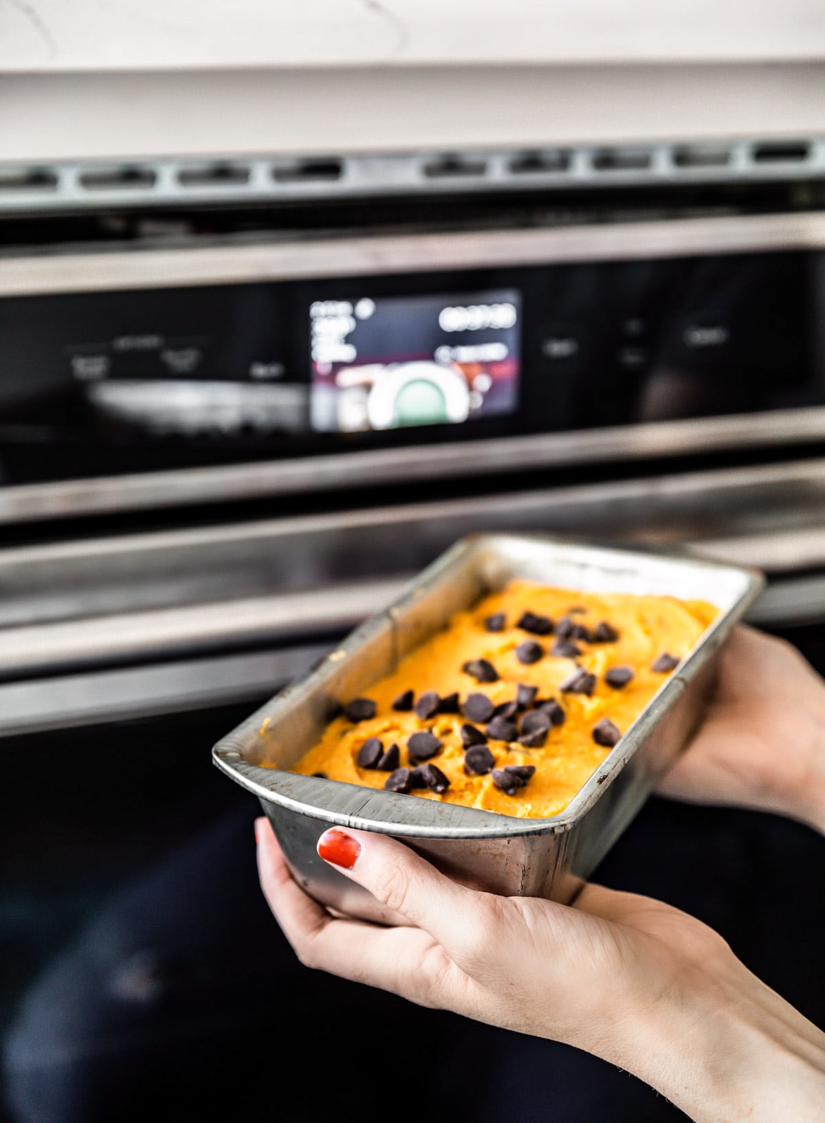 A woman's hand placing a pan of gluten free pumpkin bread batter in the oven.