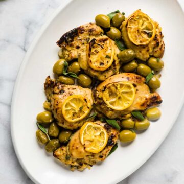 Sage chicken thighs topped with roasted lemon slices and green olives.