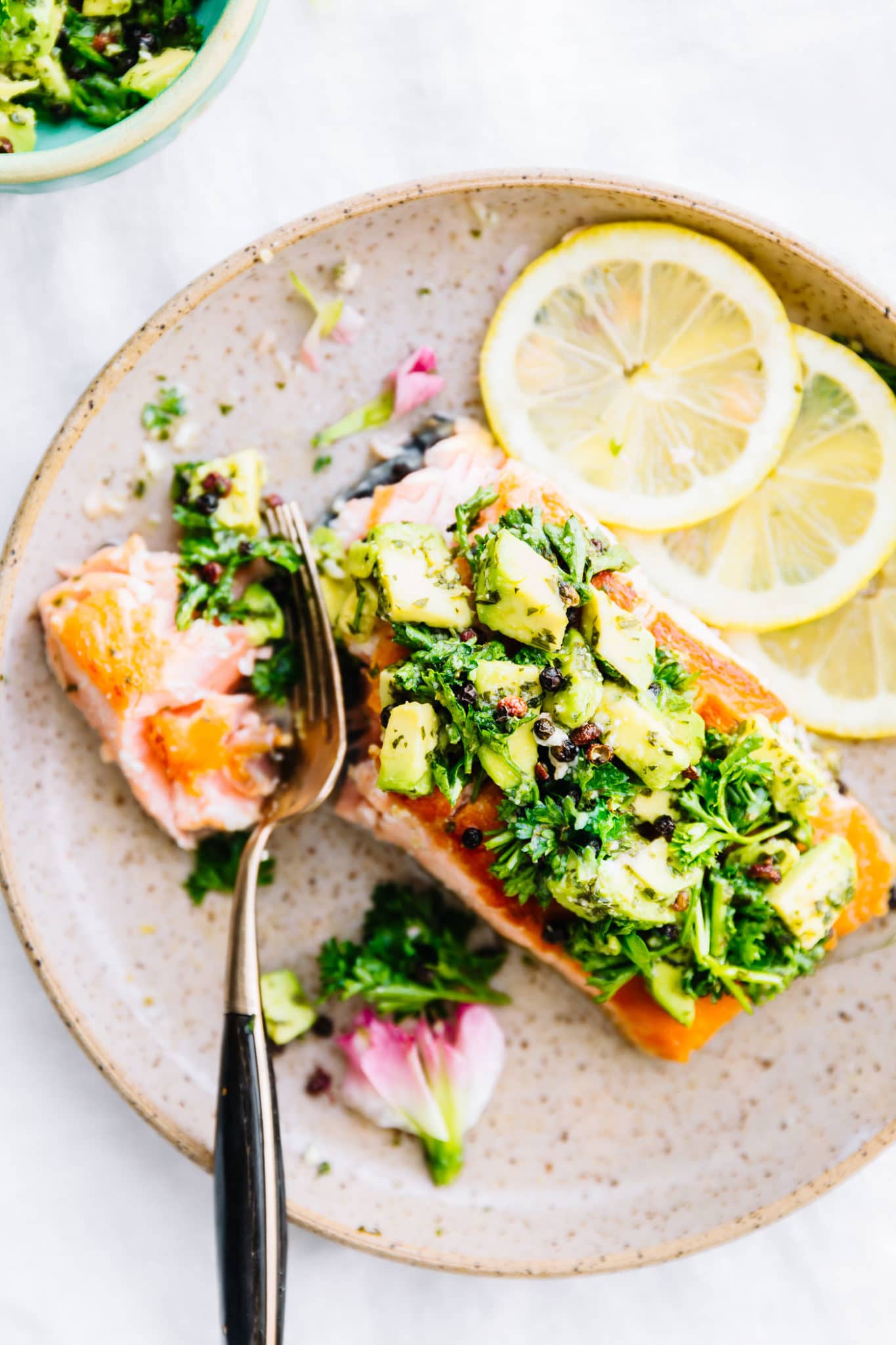 Overhead view pan seared salmon fillet topped with avocado gremolata serving on brown speckled plate.