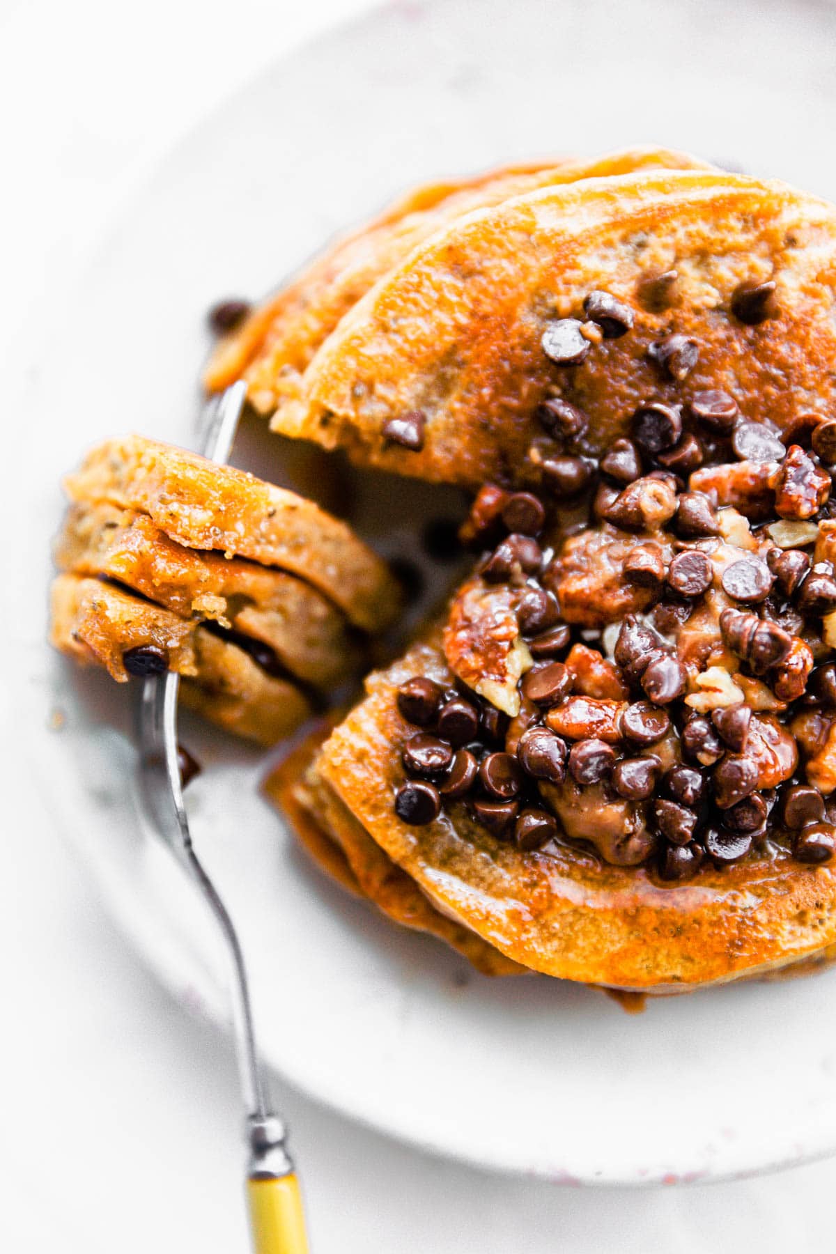 overhead image of a stack of 4-ingredient paleo pancakes topped with chocolate chips with a fork taking a bite out