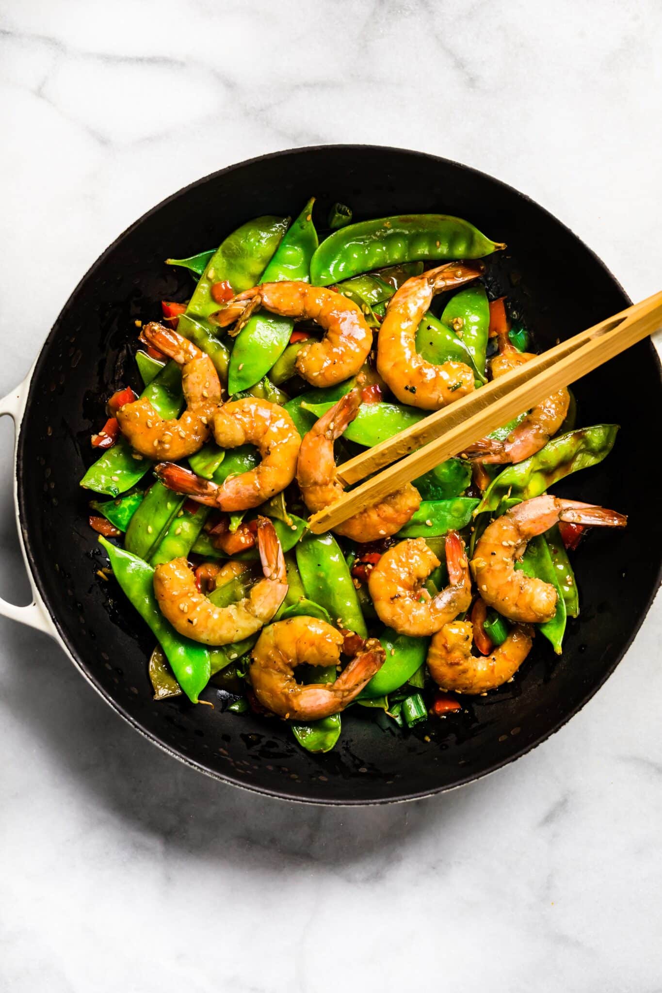 Orange shrimp stir fry in a black pan with chopsticks.