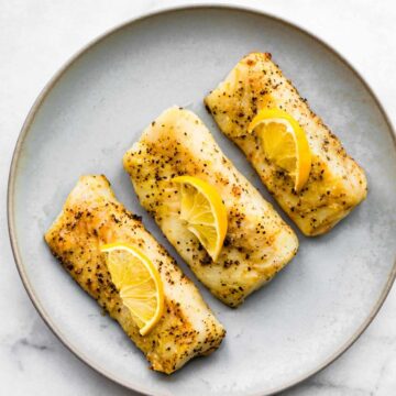 Three cooked fish fillets topped with lemon on a grey plate
