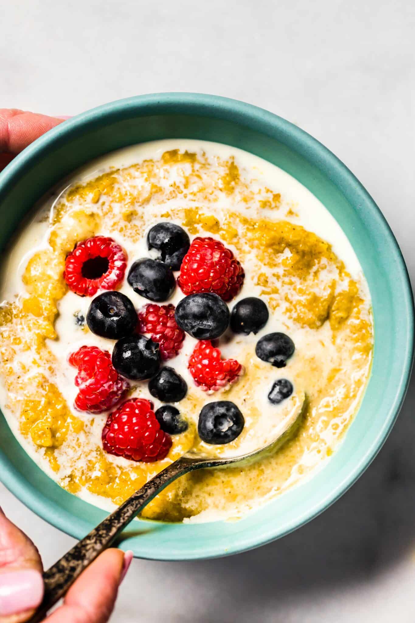 A woman holding a bowl of AIP breakfast porridge topped with berries and cream.