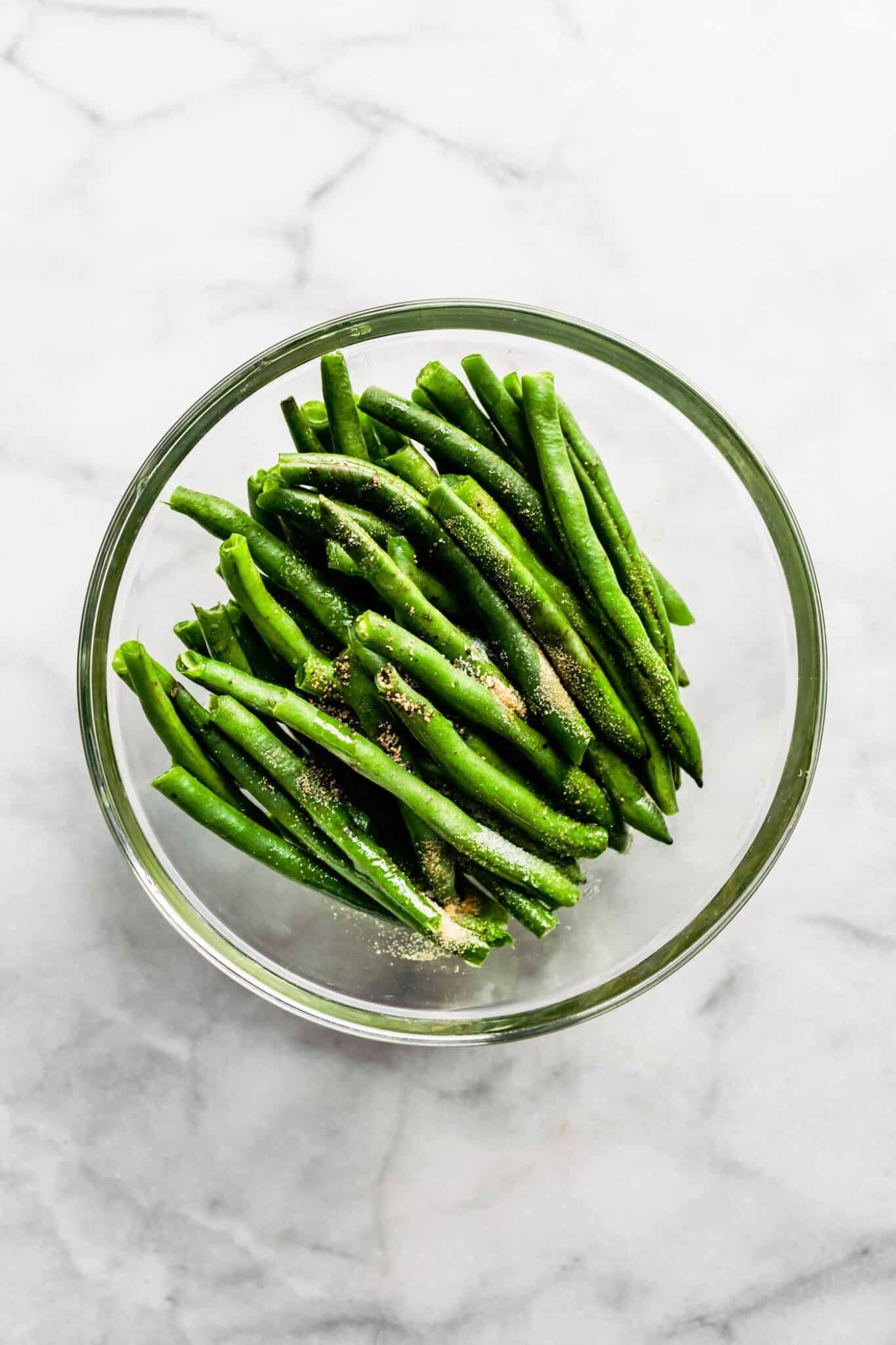 Overhead photo of fresh green beans in a bowl topped with seasonings.