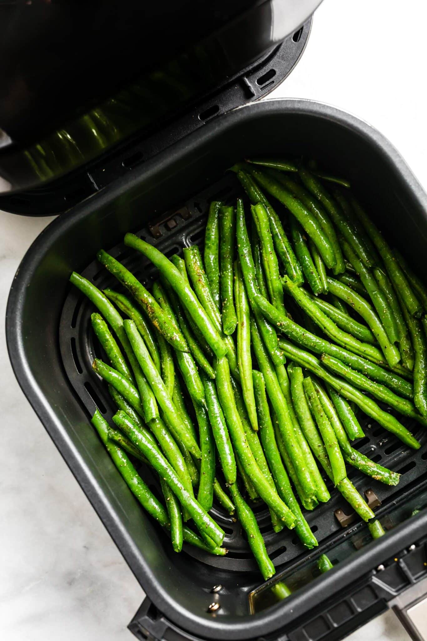 Fresh green beans in the basket of an air fryer.