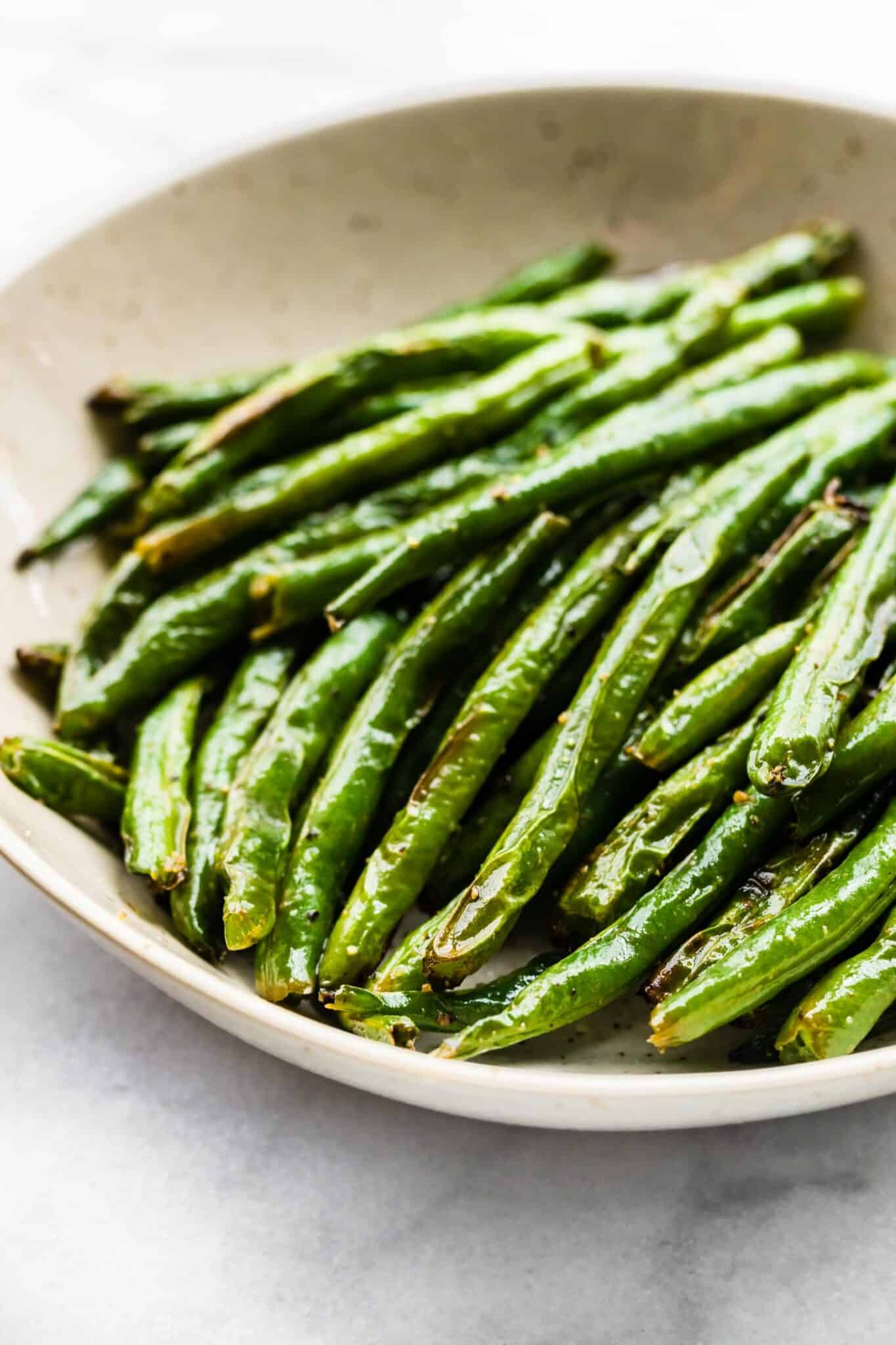 Up close photo of air fried green beans in a shallow bowl.