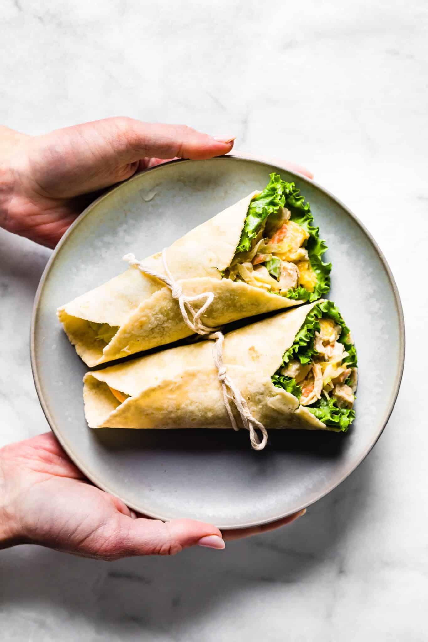 A woman's hands holding a plate with two Asian chicken salad wraps.