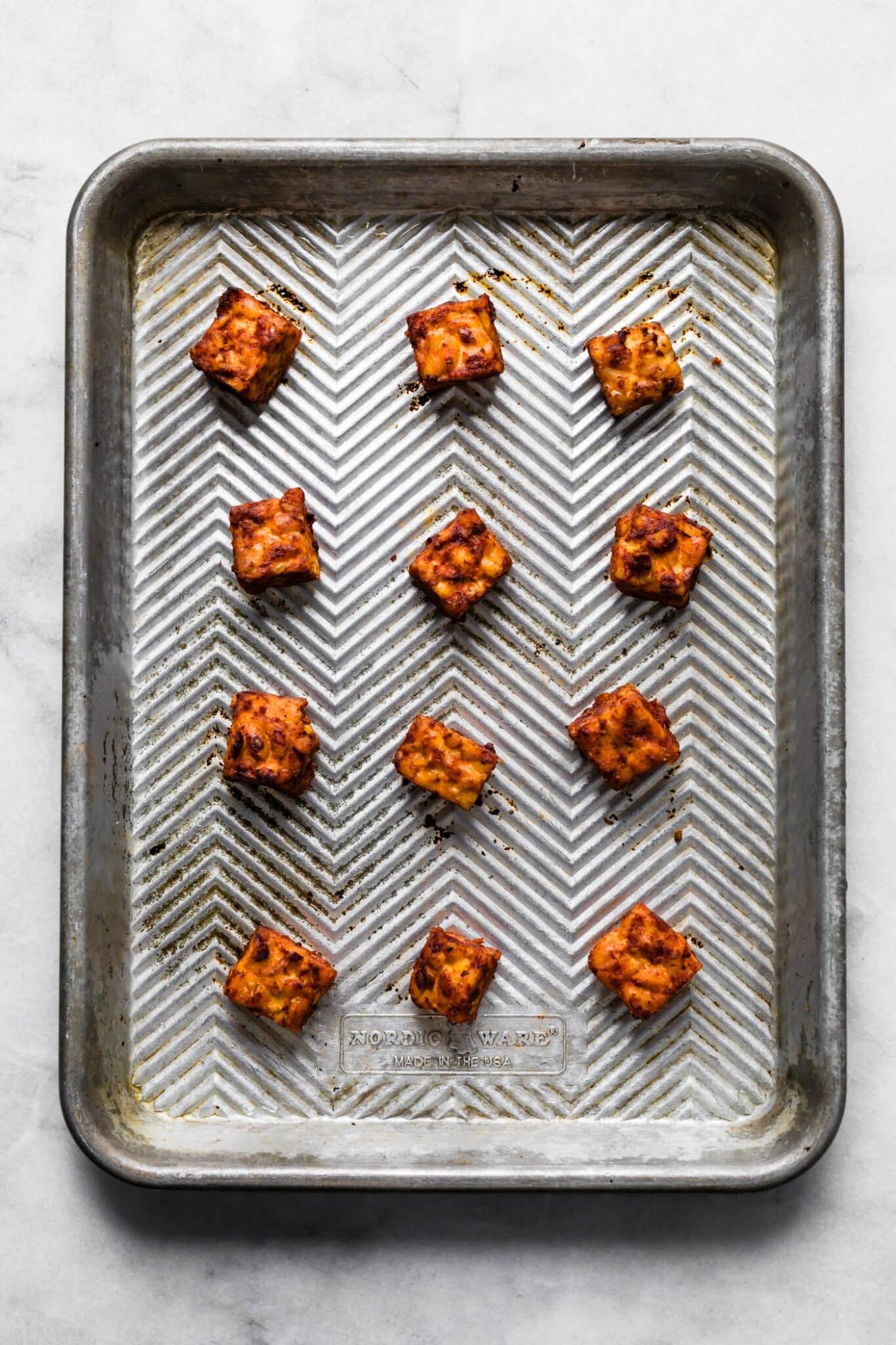 Twelve cubes of roasted BBQ tempeh on a metal sheetpan.