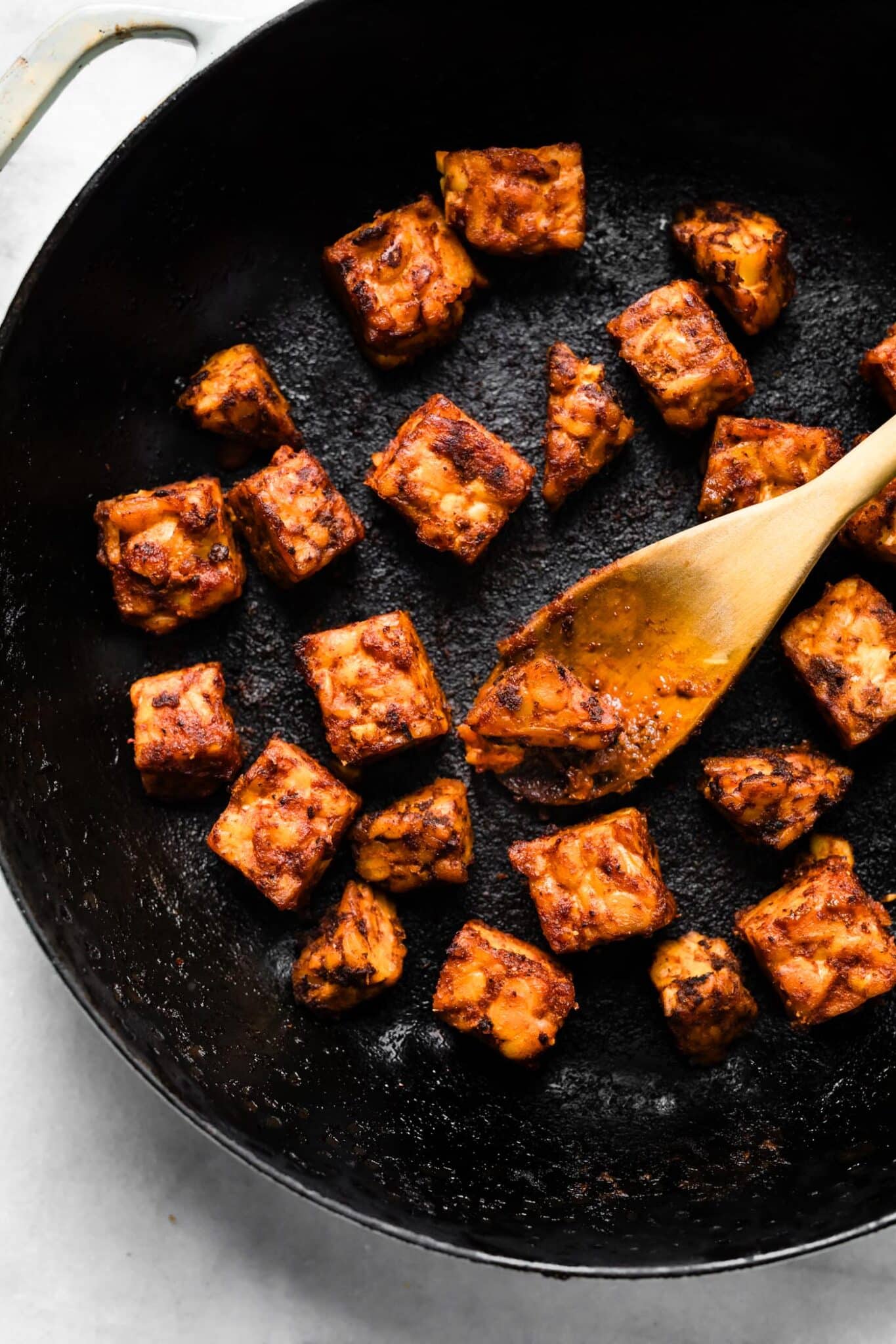 A wooden spoon in a cast iron pan with sauteed BBQ tempeh.