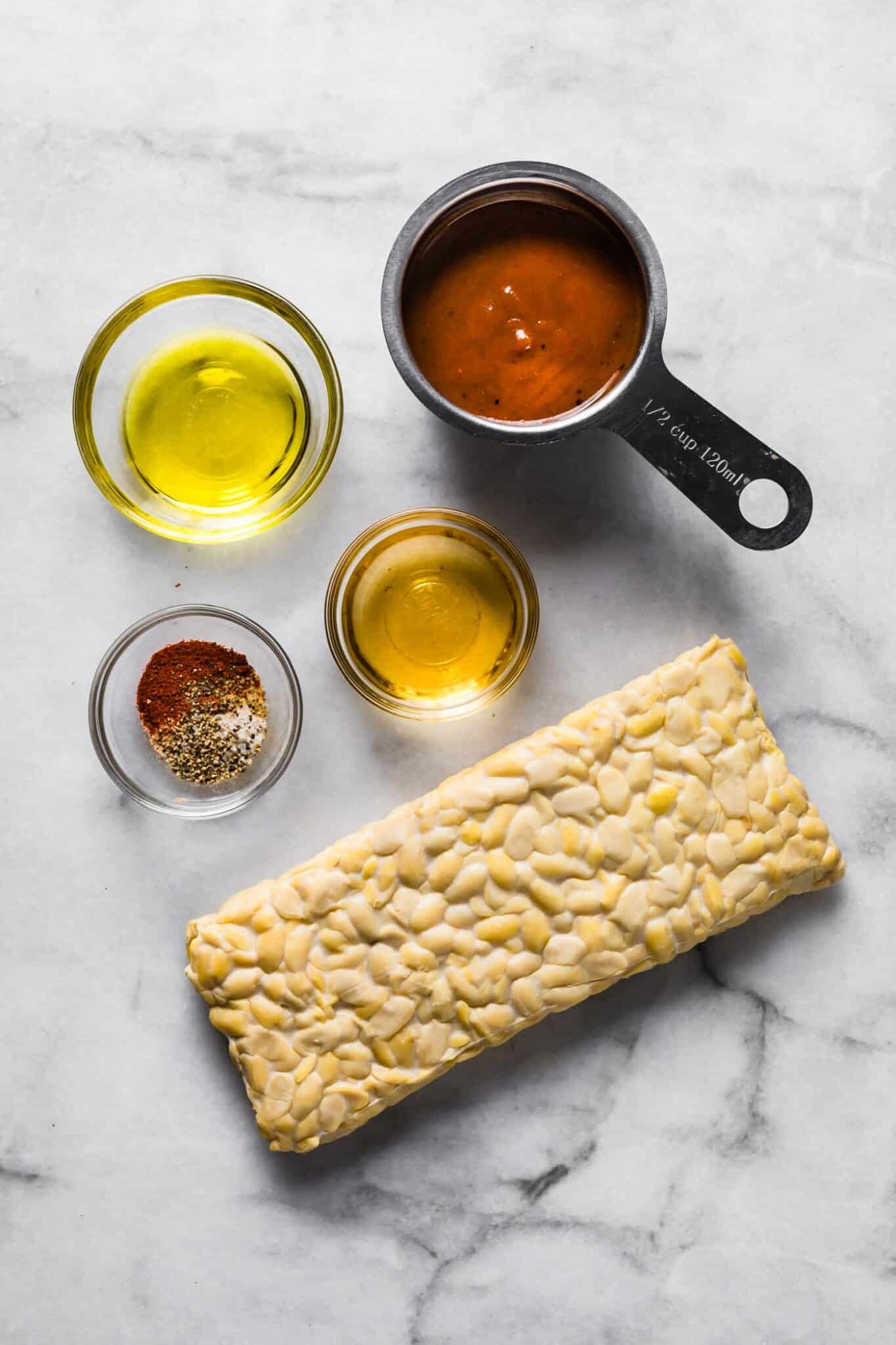 Ingredients for marinated BBQ tempeh on a white marble countertop.