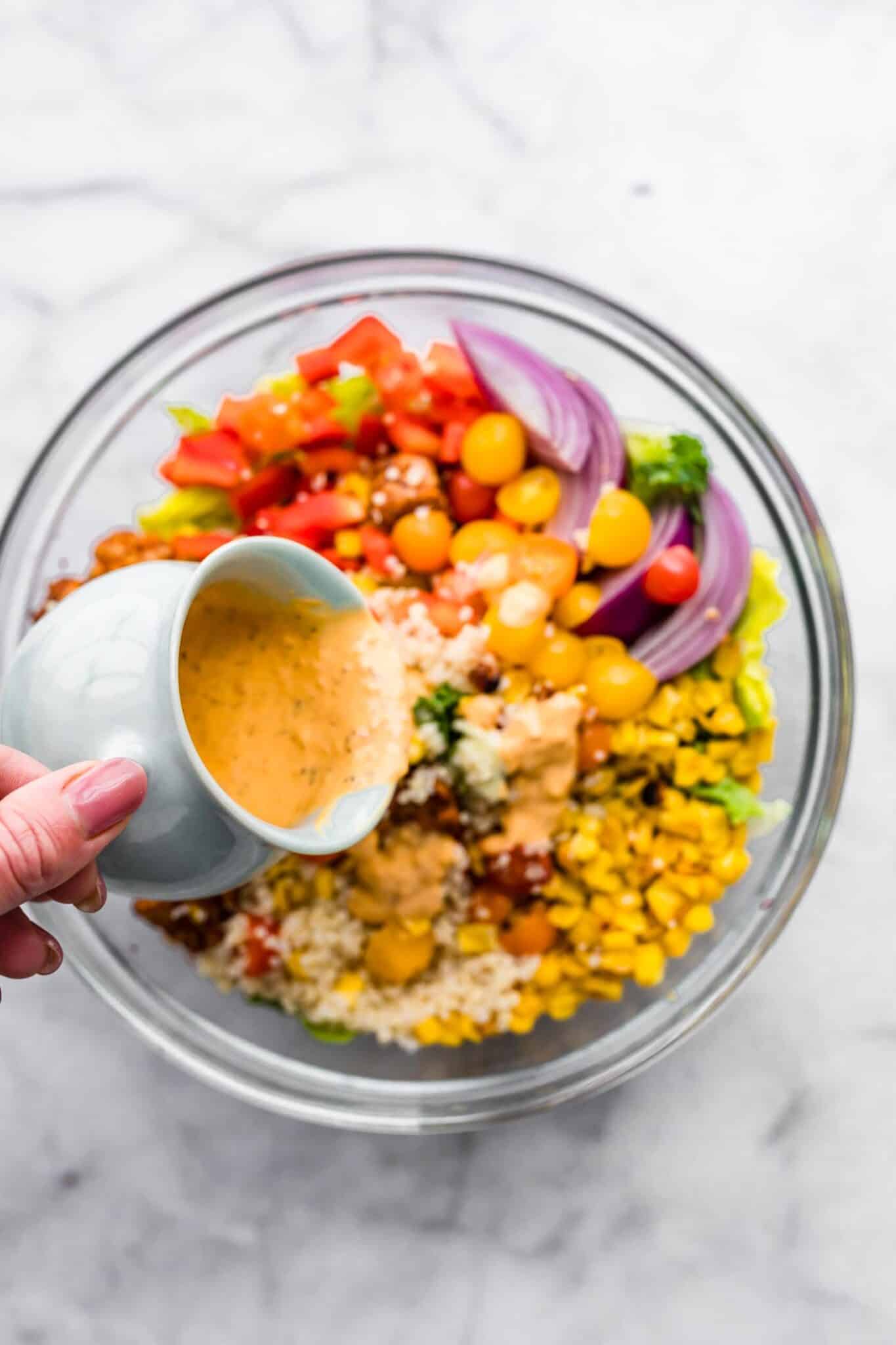 A woman's hand pouring homemade salad dressing over a colorful quinoa salad.