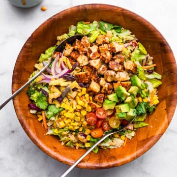 Two metal spoons in a wooden bowl filled with BBQ tempeh salad with quinoa.