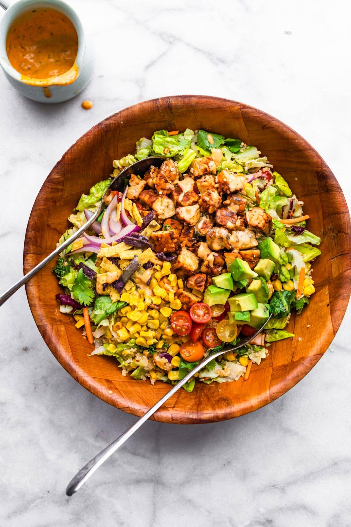 Two metal spoons in a wooden bowl filled with BBQ tempeh salad with quinoa.