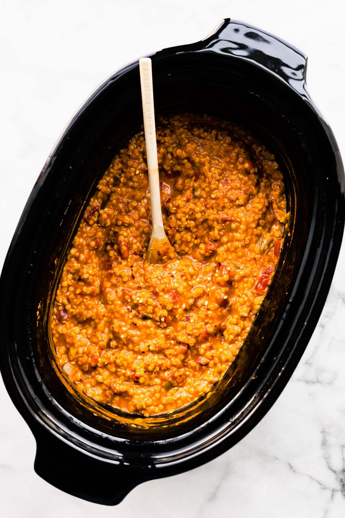 A wooden spoon in a slow cooker of vegan bbq lentil chili.