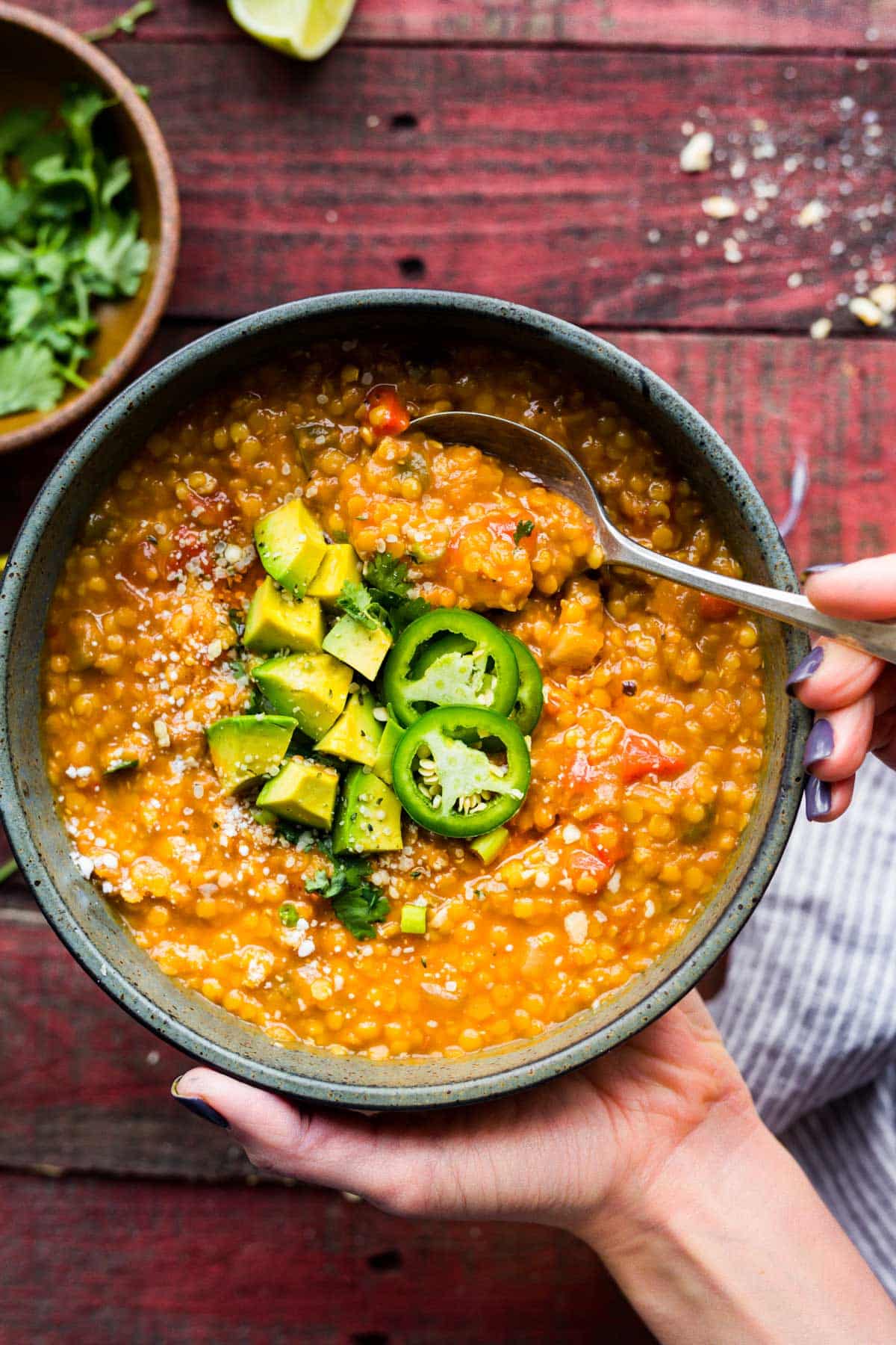 A woman's hands holding a bowl of bbq lentil chili topped with jalapeno.