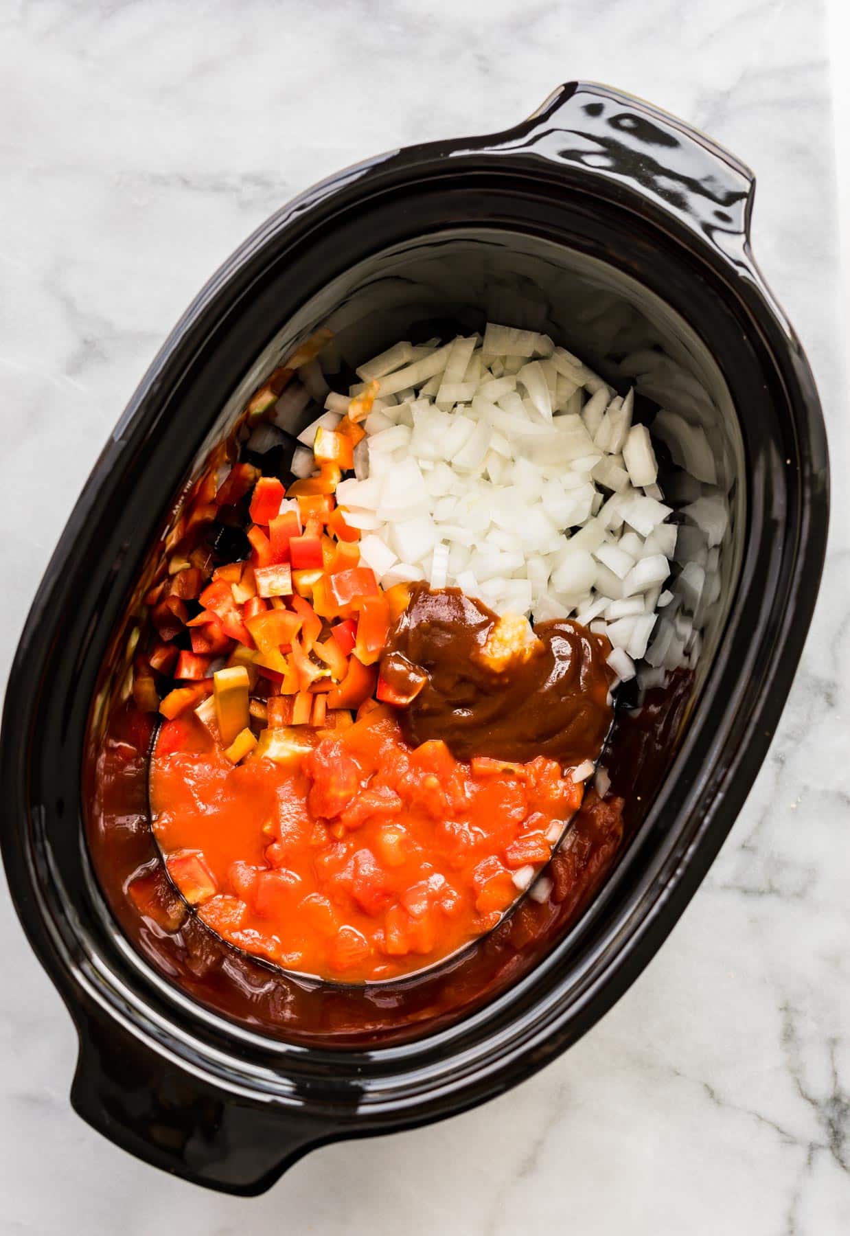 Overhead photo of diced pepper, onion, bbq sauce and diced tomatoes in a slow cooker.