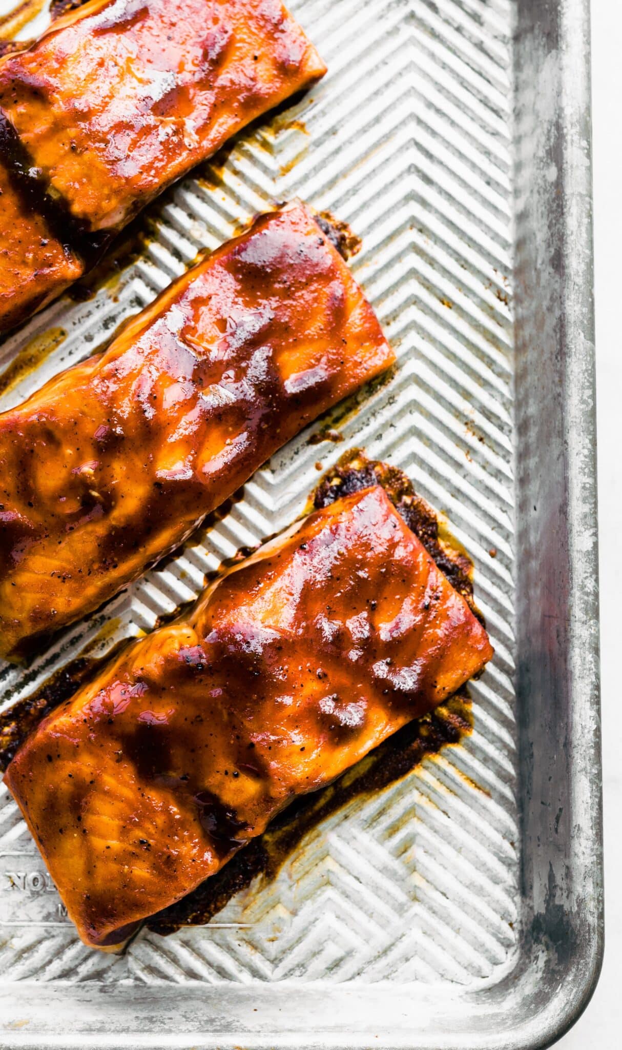 Overhead photo of BBQ sauce on salmon filets on a sheet pan.