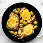 Five roasted chicken thighs in a cast iron skillet surrounded with green olives.