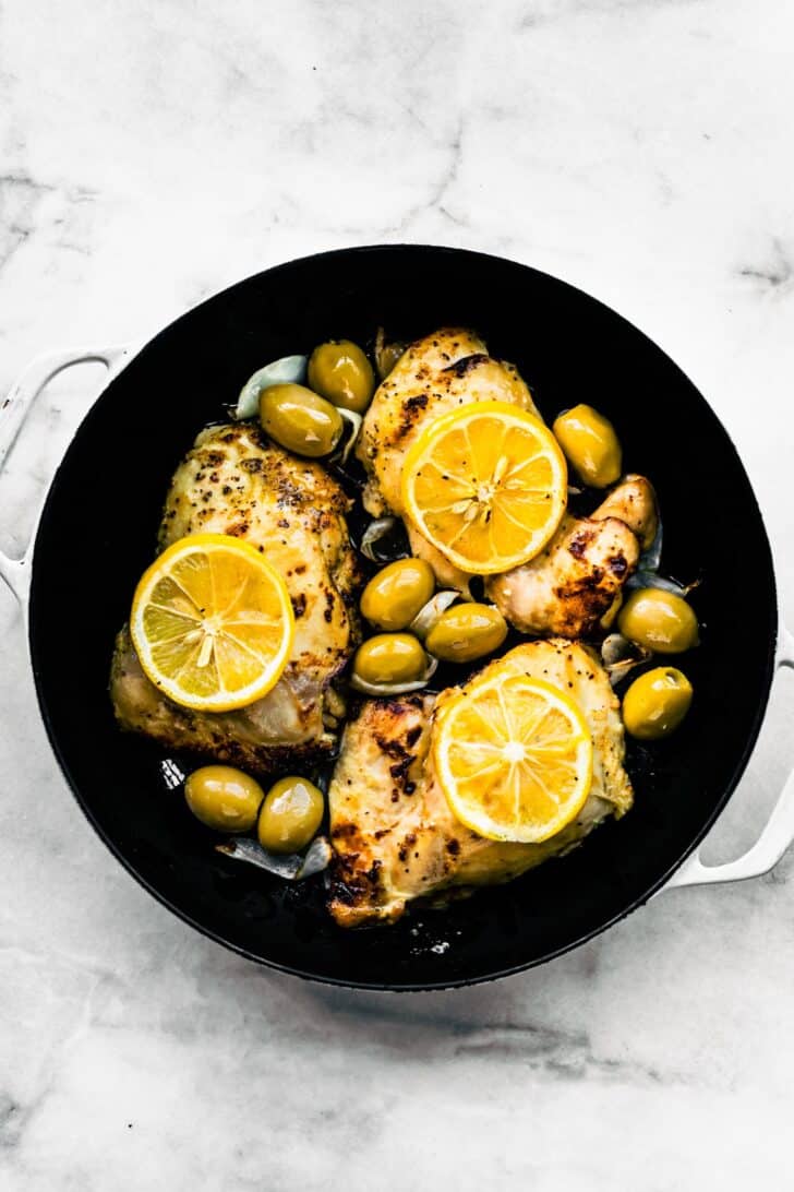Four roasted chicken thighs in a cast iron skillet surrounded with green olives.