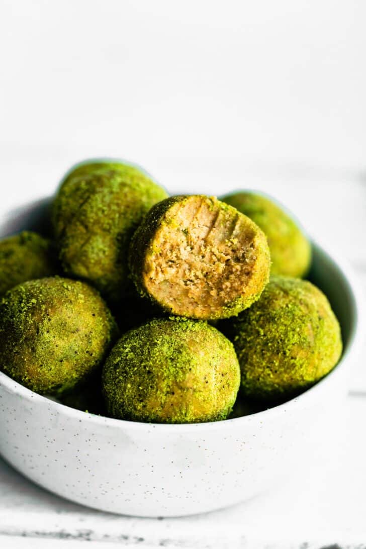 white bowl of green matcha protein bites with one bite having bite mark.