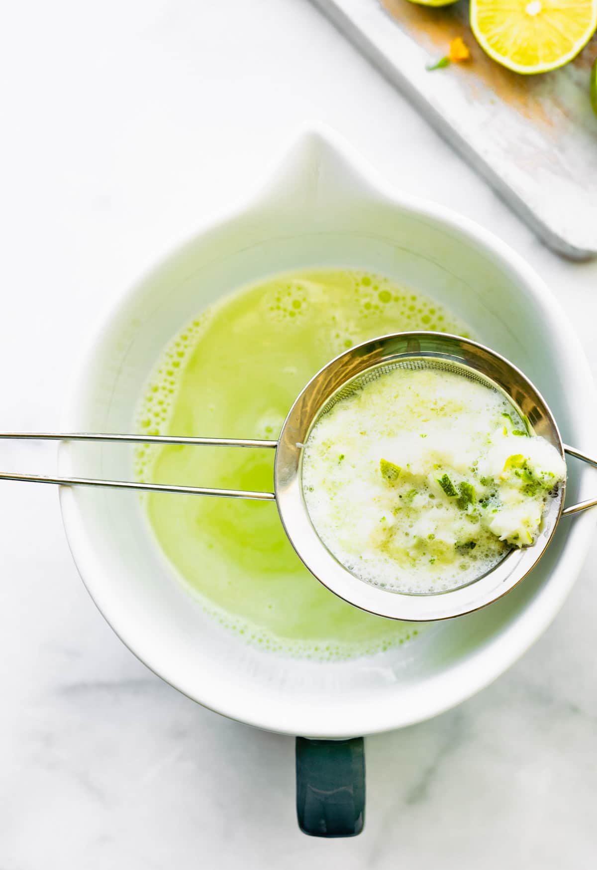 Overhead image of a fine mesh strainer with lime pulp over a white mixing bowl.