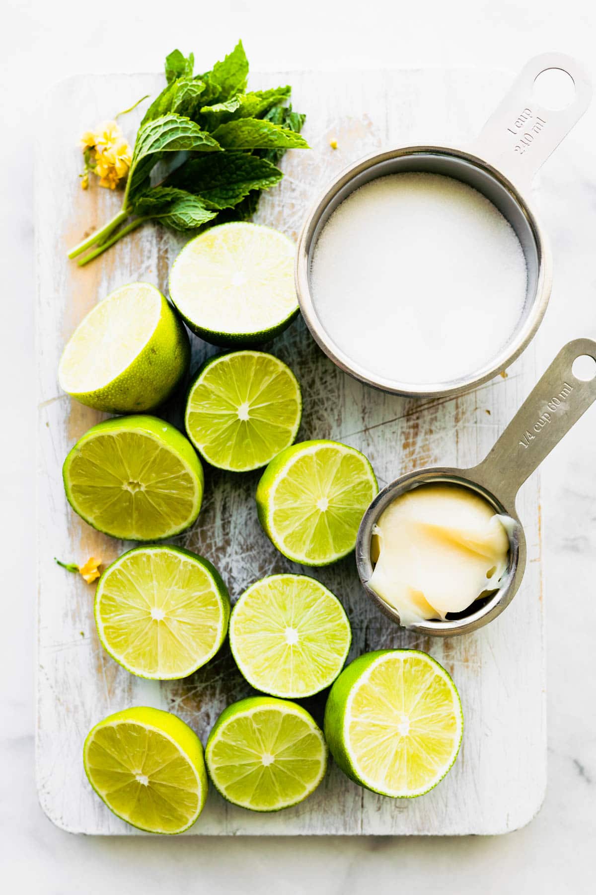 Vegan condensed milk, fresh mint and limes cut in half on wooden cutting board.