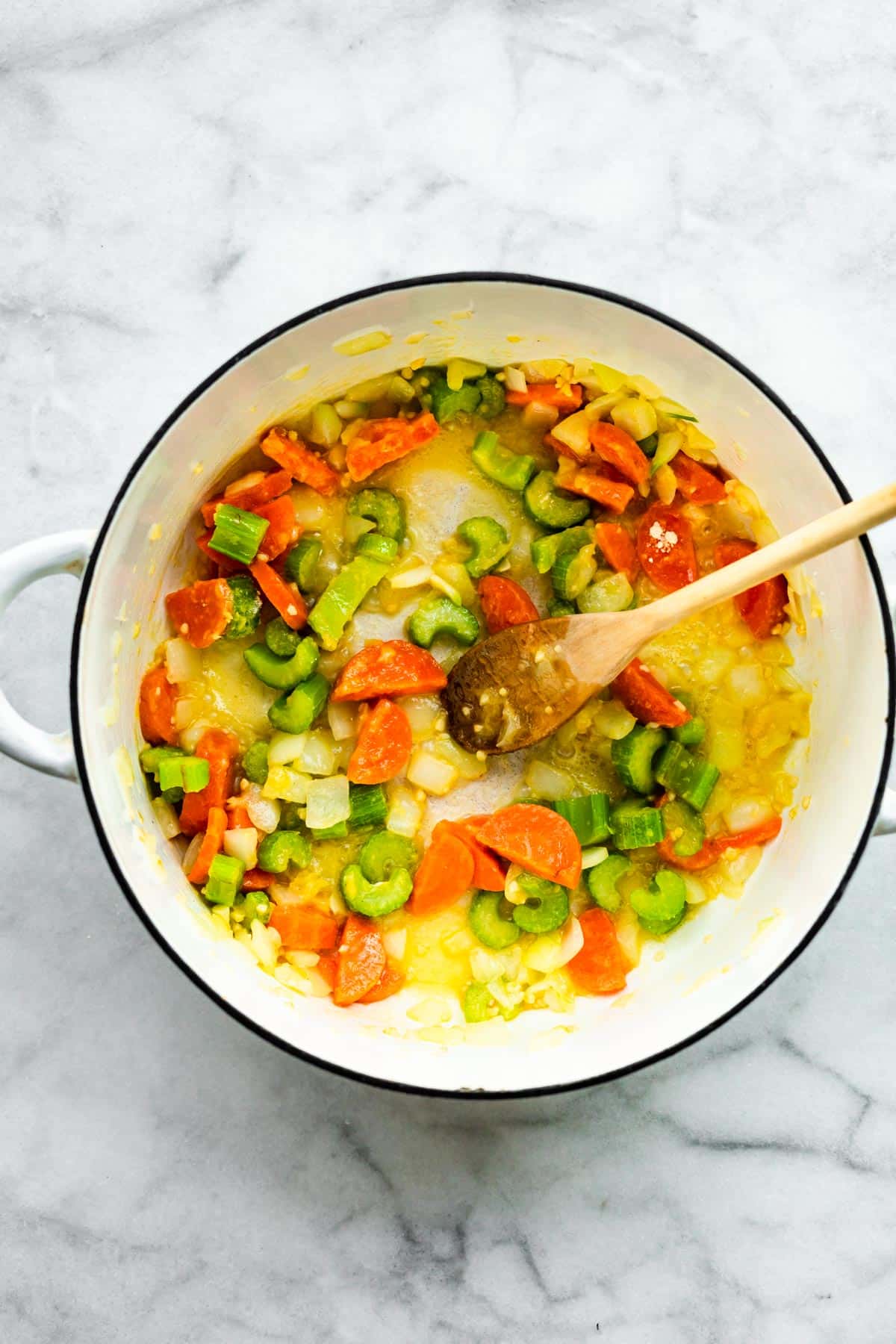 Overhead photo of a white pot of sauteed carrots, celery and onion.