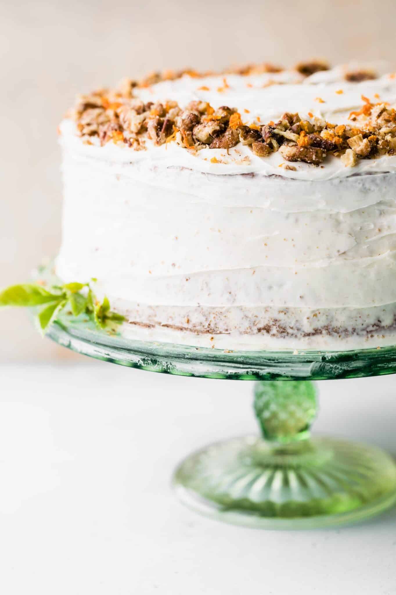 A two tiered round cake with white cream cheese frosting on a green cake stand.
