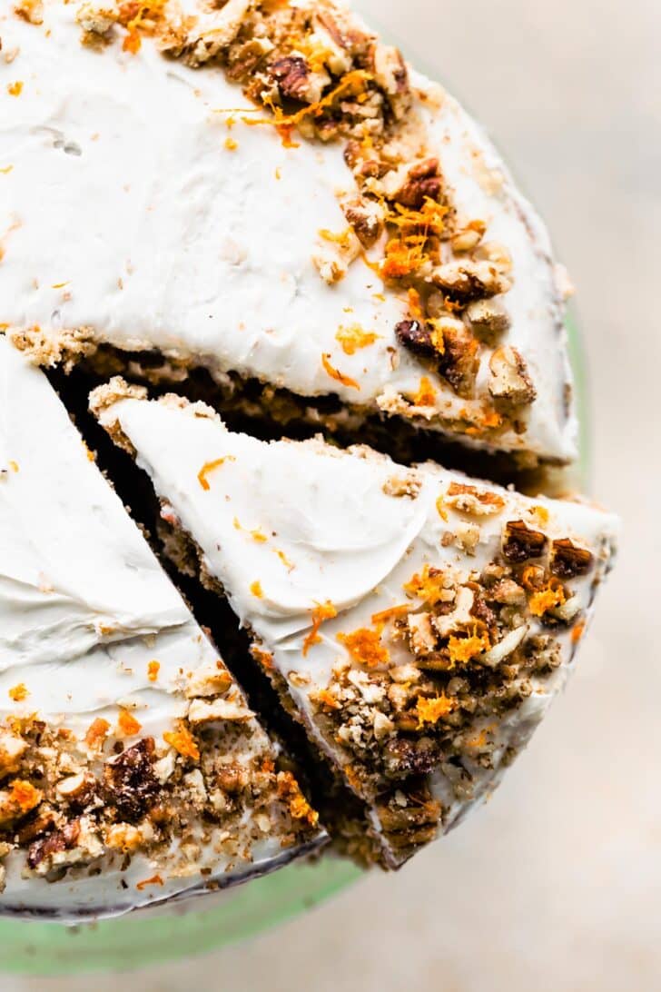 A slice of carrot cake cut out of a round cake on a cake stand.