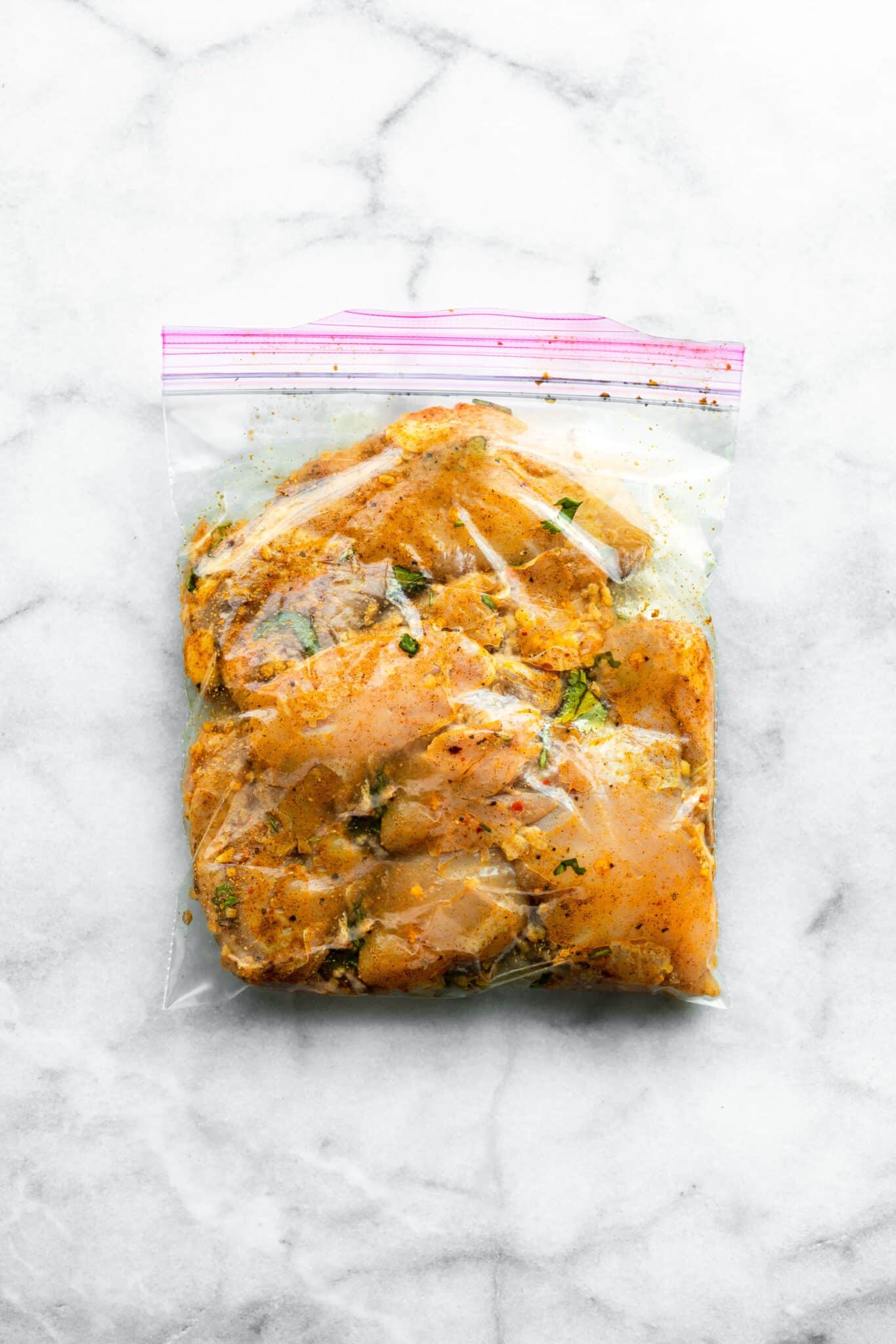 Chicken thighs marinating in a bag with shawarma spices in oil and lemon juice.