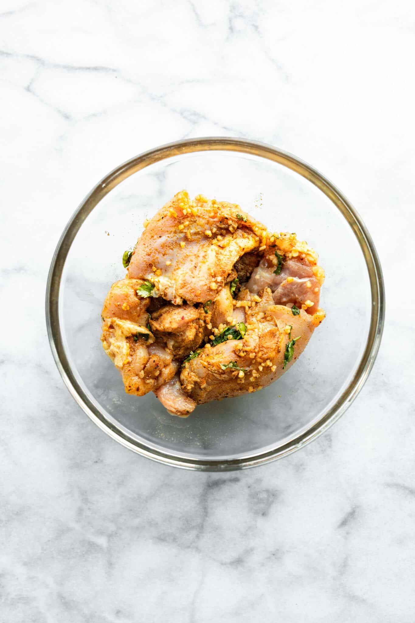 Chicken thighs marinating in a bowl with shawarma spices in oil and lemon juice.