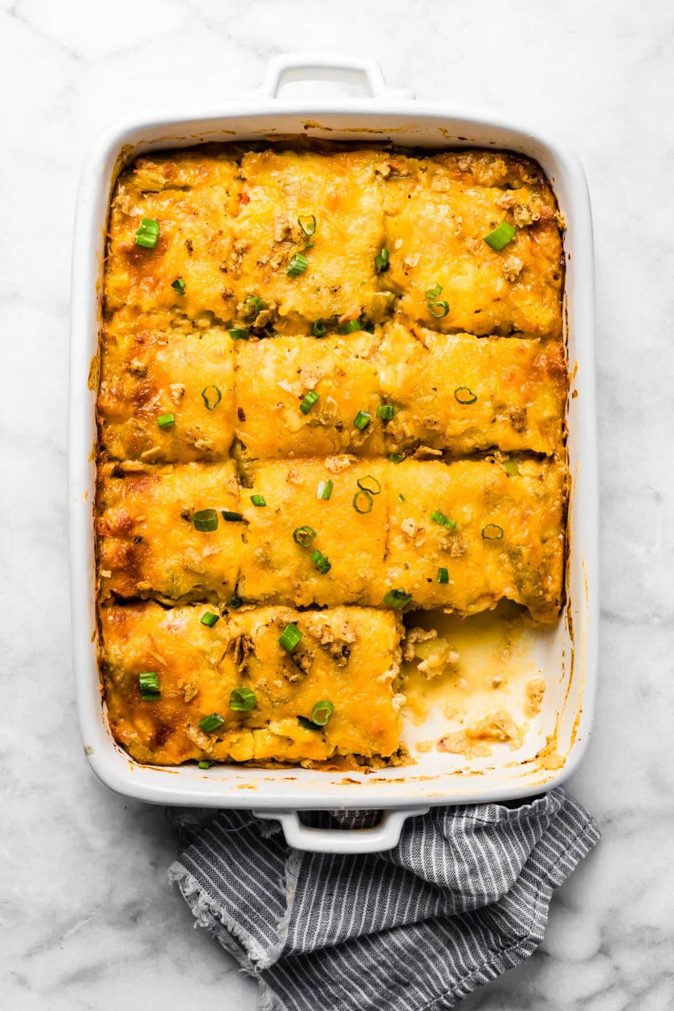 Baked potato breakfast casserole with melted cheese and green onions, one piece removed.