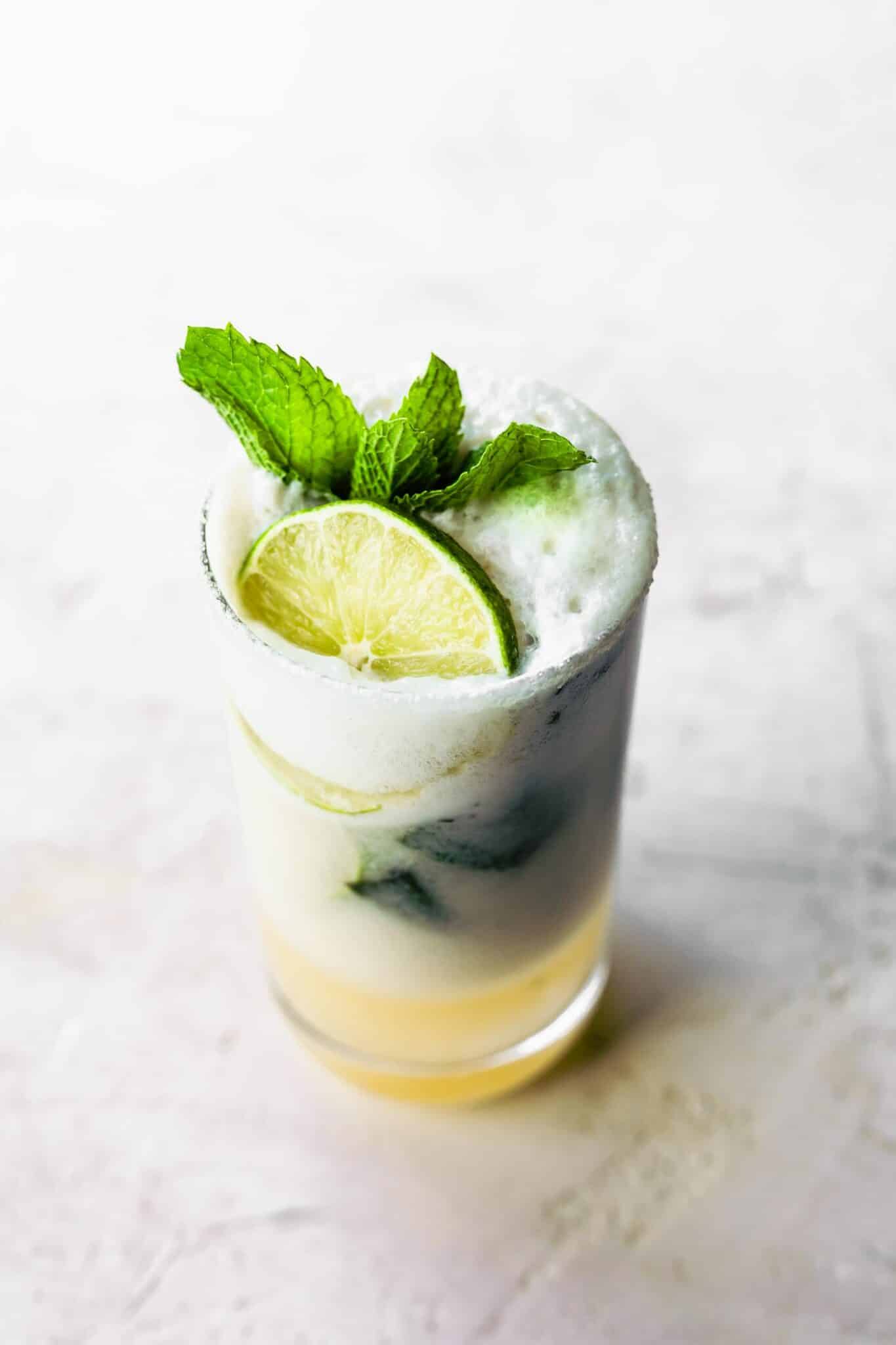 A glass filled with creamy coconut mojito topped with fresh mint leaves and lime slice.