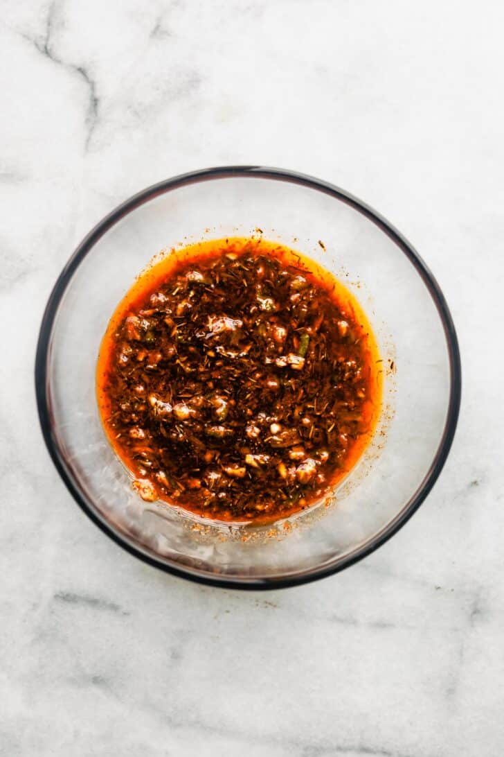 Overhead shot of jerk chicken marinade in a clear bowl, showing its red-brown color and specks of herbs.