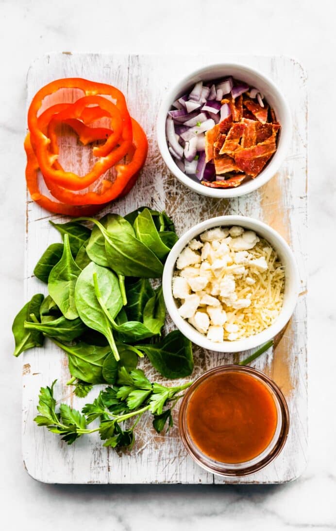 Red onions, bacon, cheese, hot sauce, red pepper, spinach, and arugula separated and ready to be added to frittatas.