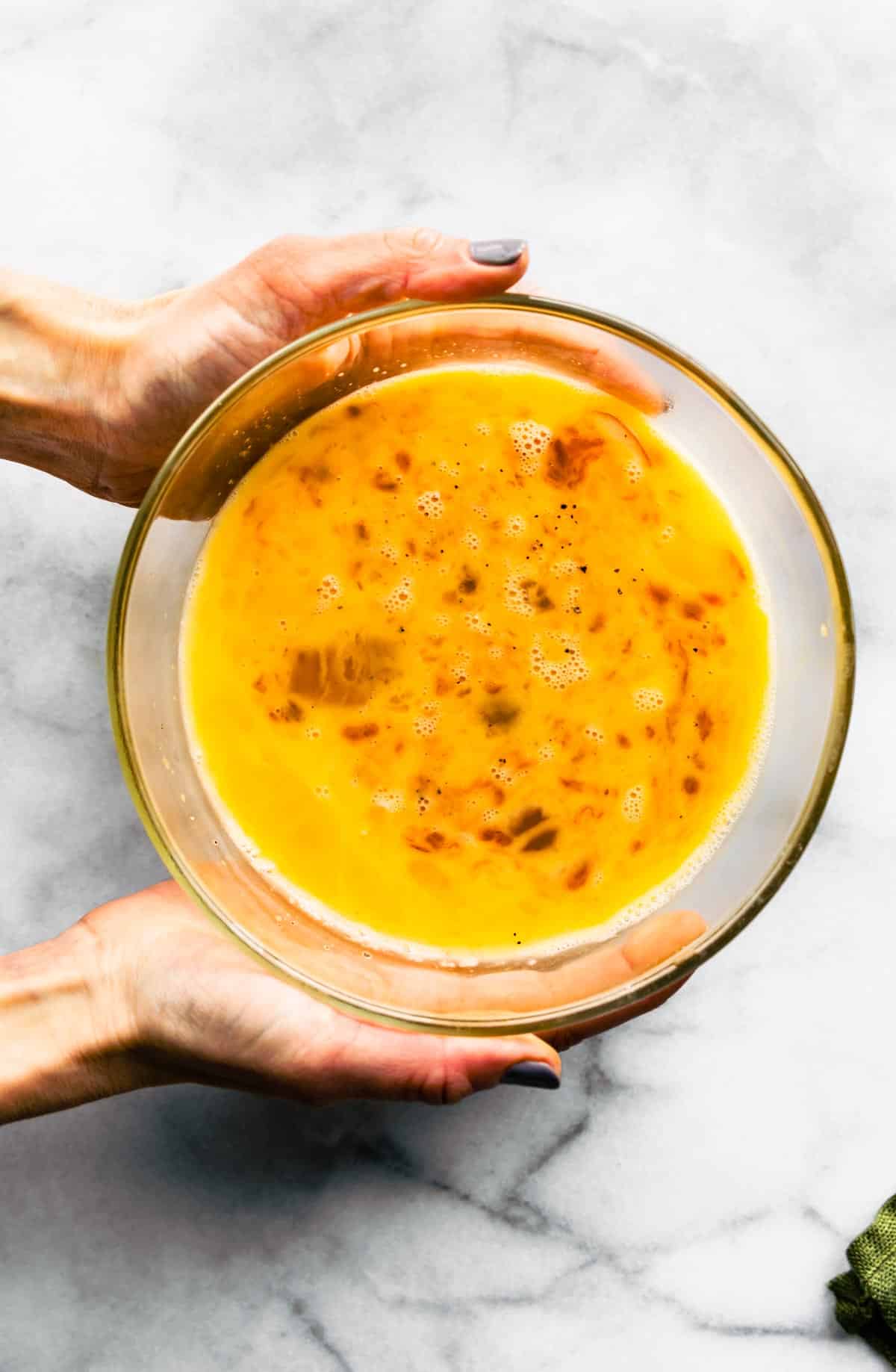 Frittata egg base in a glass bowl being held by hands.