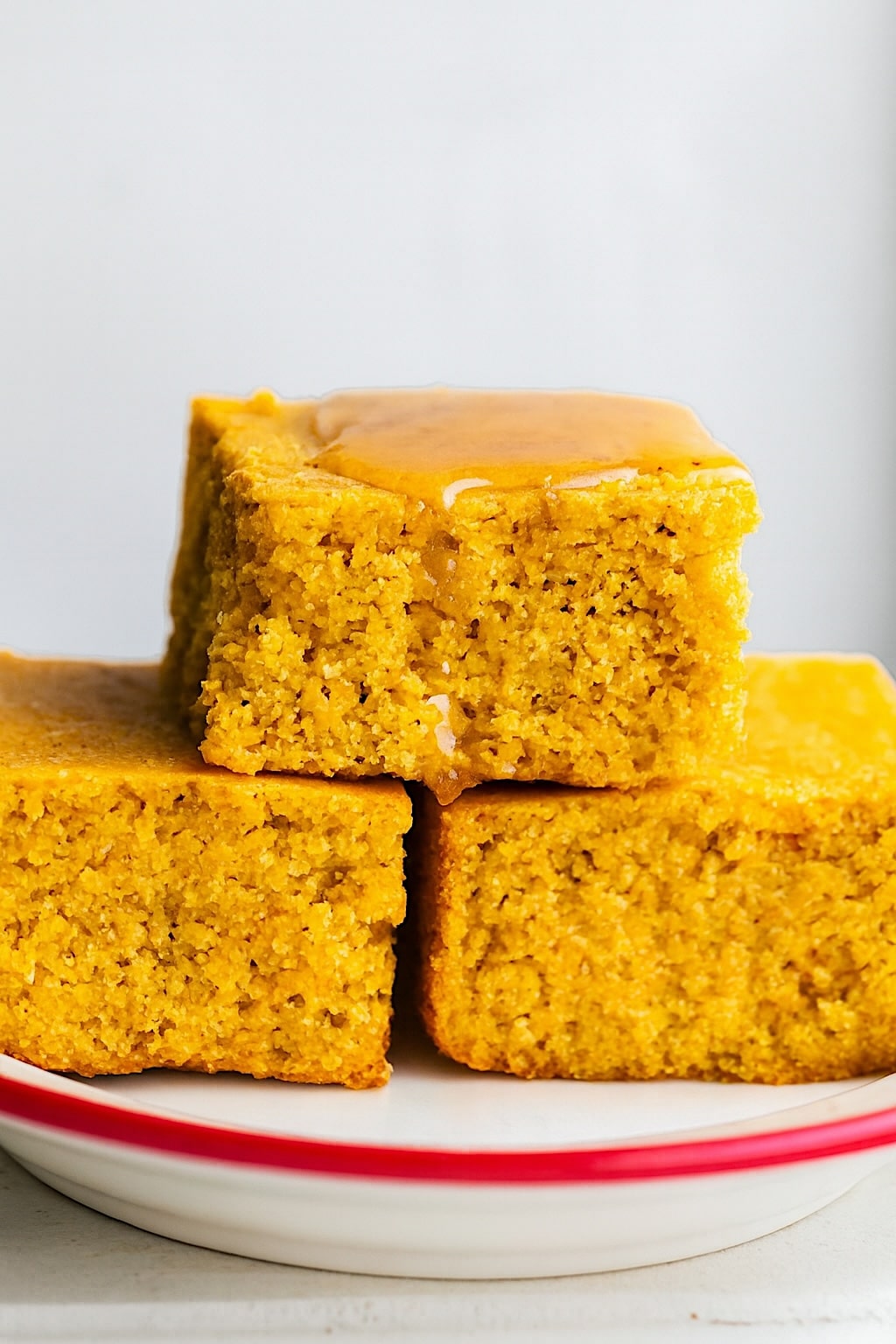 Stacked squares of gluten-free cornbread with a drizzle of honey on top on a red and white plate